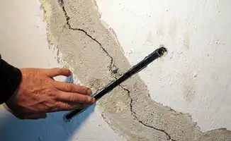 A wall with a large crack is being inspected by a professional in Jersey City, NJ
